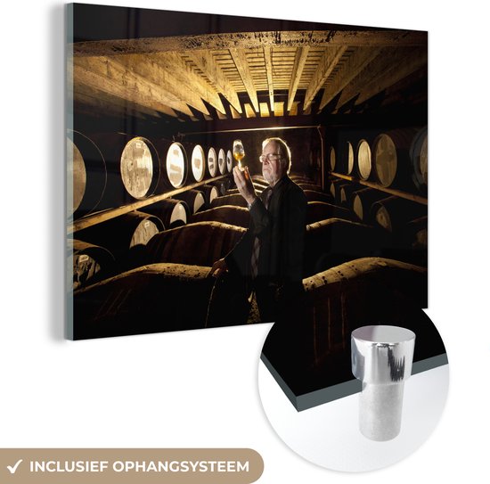 MuchoWow® Glasschilderij 60x40 cm - Schilderij acrylglas - Man test whisky tussen houten vaten in de kelder van distelleerderij - Foto op glas - Schilderijen