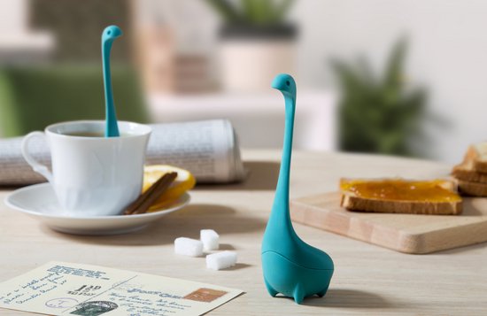 Turquoise dinosaurus-vormige theefilter op een houten tafel met toast en post.