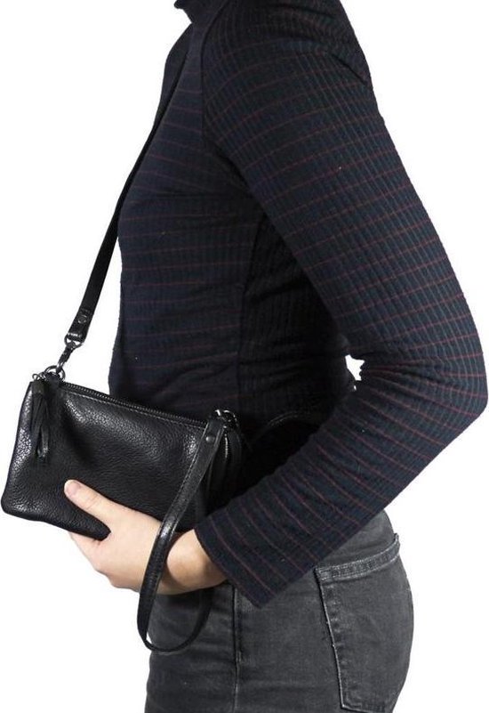 Zwarte leren clutch met polsbandje, gedragen door een model met een zwart gestreept shirt.