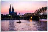 PVC Schuimplaat - Uitzicht op de Dom en Brug van Keulen tijdens de Avondzon in Duitsland - 60x40 cm Foto op PVC Schuimplaat (Met Ophangsysteem)