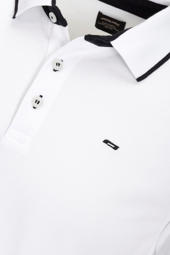 Detail van witte polo met zwarte bies, knopen en logo.