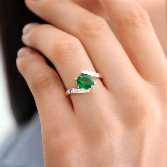 Damesring met een groene steen op de hand, met kleine witte steentjes op de band.