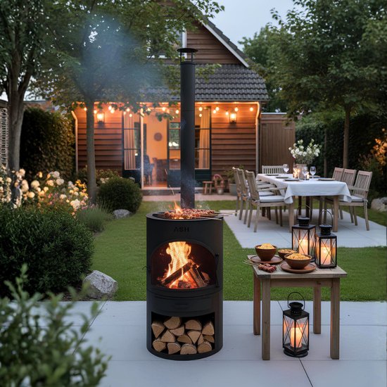 Zwarte tuinhaard met brandend vuur, houtopslag, bijzettafel met eten en tuinmeubilair.
