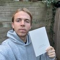 Jonge man in grijze hoodie houdt een wit notitieboekje vast met de tekst 'Growth Journal'.