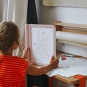 Kind met oranje gestreepte kleding houdt roze lichttablet met getekende prinses.