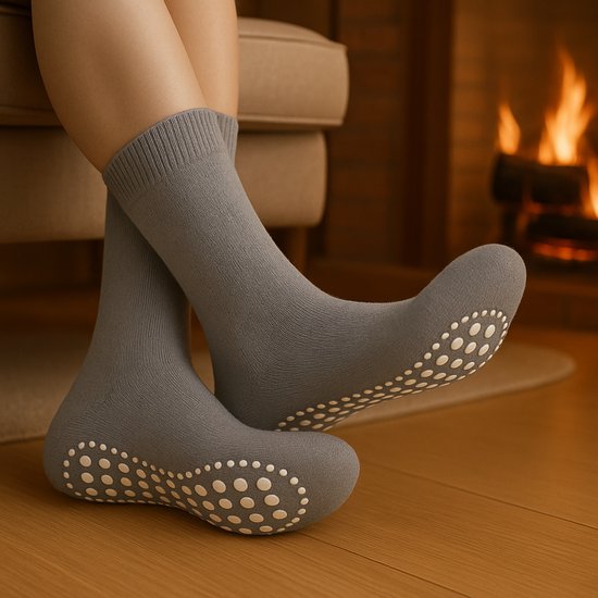 Grijze huissokken met witte antislip noppen op de zolen, gedragen bij een haardvuur.
