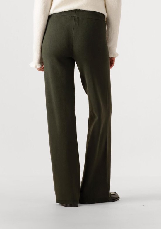 Achterkant van een vrouw in donkergroene broek met witte cardigan.