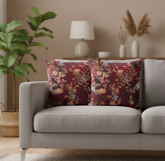 Twee bordeauxrode sierkussens met bloemenprint op een grijze bank.