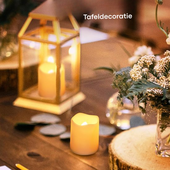 Een witte LED-kaars staat op een houten tafel, naast een gouden lantaarn en bloemen, met de tekst 'Tafeldecoratie'.