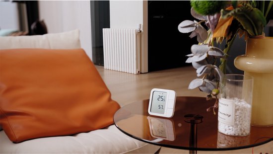 Witte slimme thermostaat op een salontafel met een digitaal display, naast een radiator.