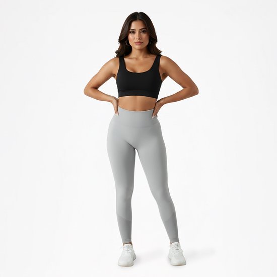 Model in grijze scrunch butt legging en zwarte sportbeha, staand met handen op de heupen.