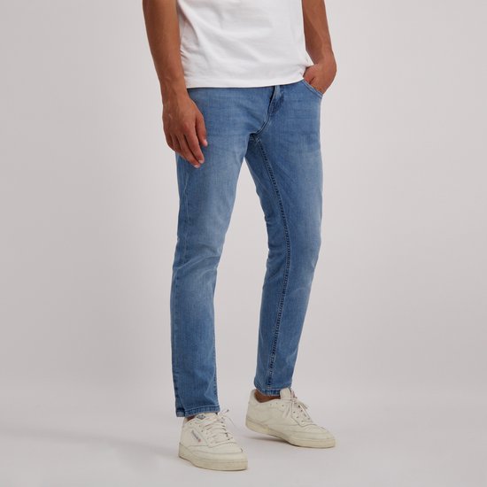 Een man met een witte t-shirt en een regular fit jeans met lichte wassing. Hij draagt witte sneakers.