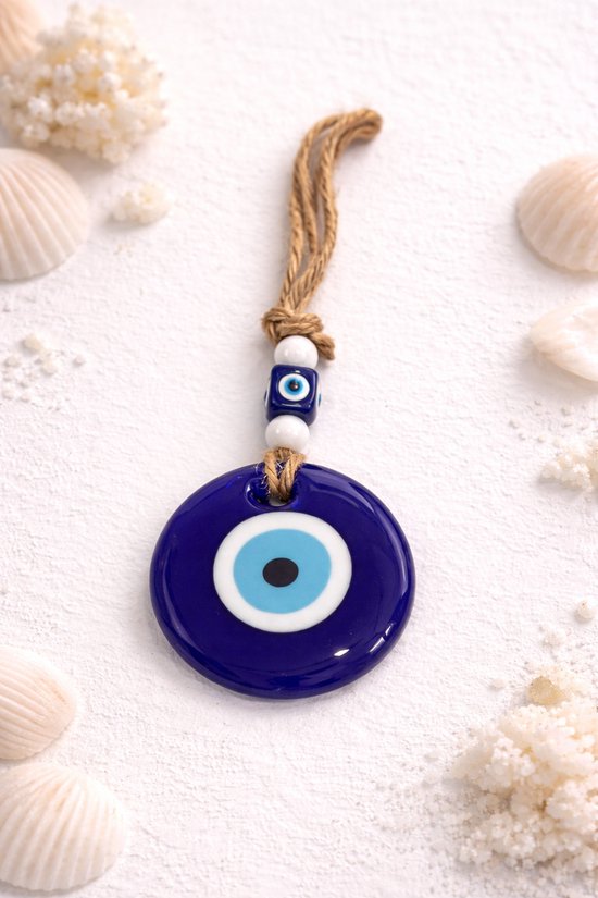 Donkerblauwe boze oog hanger met touw, omringd door schelpen en zand.