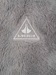 Wit driehoekig logo met 'BJØRNSON' erop, op een grijze fleece achtergrond.