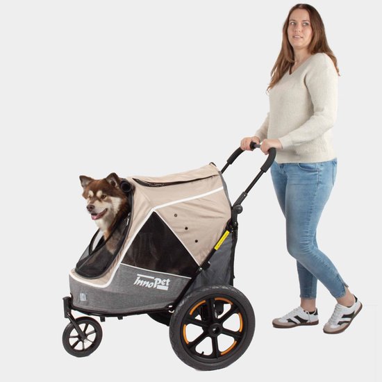 Vrouw duwt beige en grijze hondenbuggy met bruine hond, met grote luchtbanden.