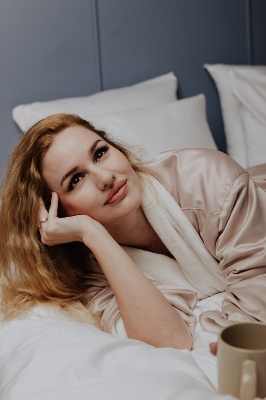 Vrouw met lang blond haar, liggend op een bed in een satijnen badjas.