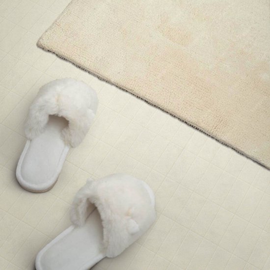 Witte pluizige slippers op een romige, betegelde vloer naast een beige badmat.