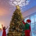 Gouden kerstboomster met projectie van sneeuwvlokken, bekroont een kerstboom versierd met kinderen.