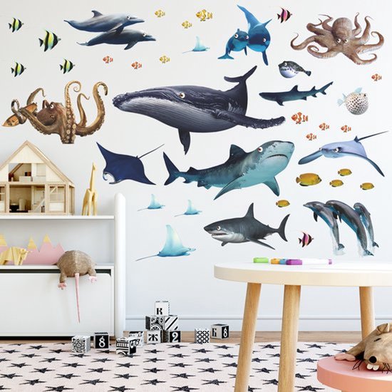 Autocollants muraux d'animaux marins, dont une baleine, des requins, des pieuvres, des raies et des dauphins, appliqués sur un mur avec des meubles de chambre d'enfant.