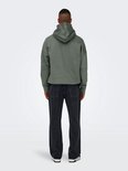 Man van achteren gezien, met een groene hoodie en wijde, zwarte spijkerbroek met stonewashed look.