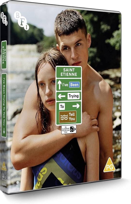 Een stel omhelst elkaar bij een stroompje, met een groen bord met de tekst 'SAINT ETIENNE I've Been Trying To Tell You'.