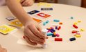 Hand van een kind die een zandloper omgedraaid houdt, bij het spel LEGO Brick Like This! met steentjes en kaarten.