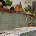 Saliegroene metrotegels met lichte textuur op de achterwand van een keuken, met gouden kraan en accessoires.