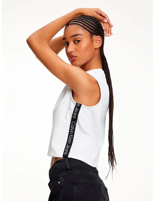 Model in wit mouwloos T-shirt met Calvin Klein Jeans logo tape op de zijkant, gecombineerd met zwarte jeans.