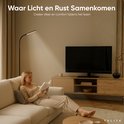 Een vrouw leest een boek op een bankje, verlicht door de TULITE Arcus Vloerlamp in een woonkamer.