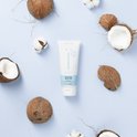 Naïf Cleansing Wash Gel met kokosnoten en katoenbloemen op een blauwe achtergrond.