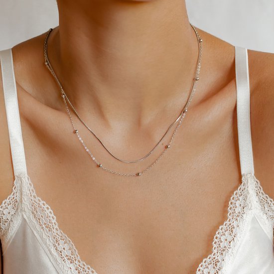 Twee zilverkleurige kettinkjes, één met slangenketting en de ander met kleine bolletjes, gedragen door een model.