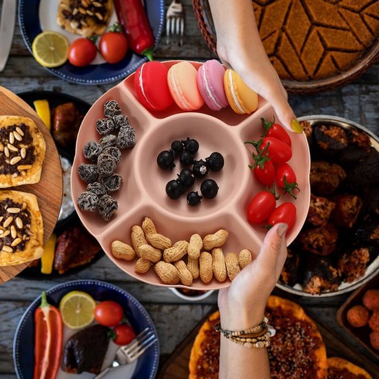 Roze snackbord gevuld met macrons, bessen, kerstomaatjes en pinda's, vastgehouden boven een tafel.