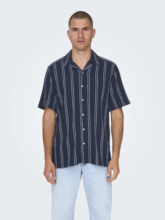 Man met een donkerblauw, verticaal gestreept kort overhemd en een lichtblauwe spijkerbroek.