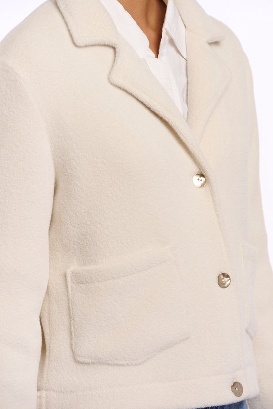 Détail d'une veste courte couleur crème avec col revers, boutons dorés et poche à rabat.