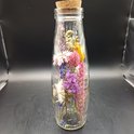 Glazen fles met kurk, gevuld met gedroogde bloemen. Roze, paarse, blauwe en witte bloemen.