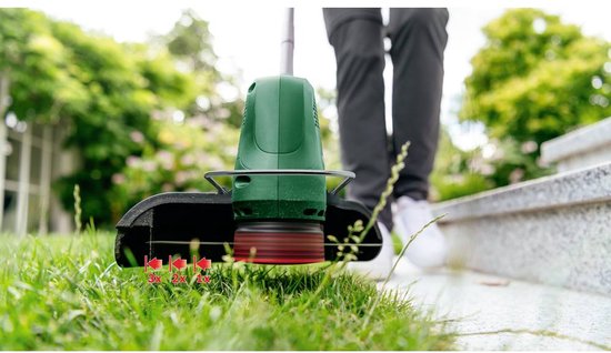 Close-up van de Bosch EasyGrassCut 18V-230 grastrimmer die gras maait, lage hoek.