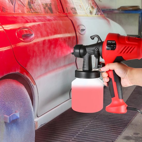 Hand houdt rode elektrische verfspuit met witte beker, spuit rode verf op een auto.