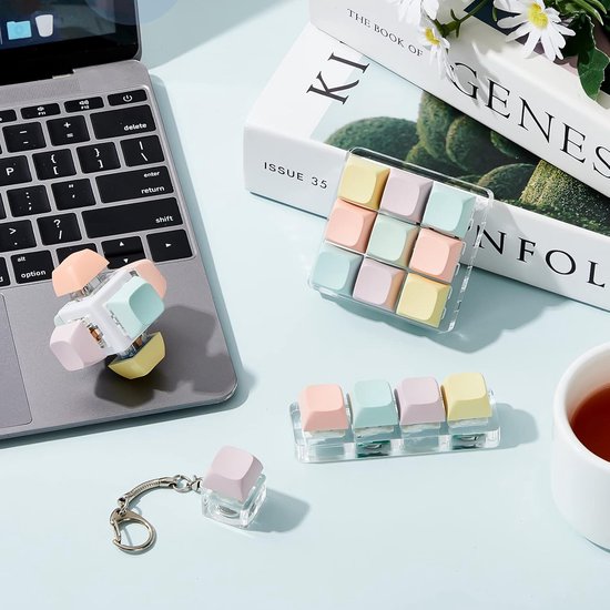Macaronkleurige keycaps op acryl display, sleutelhanger en kubusvormige fidget toy naast een laptop.