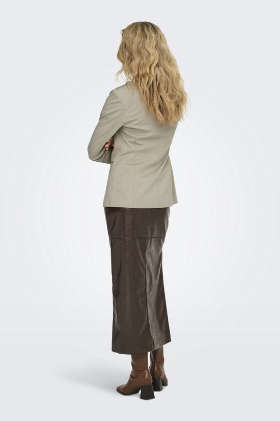Model staat met de rug naar de camera in een beige blazer, wit shirt en bruine leren rok.