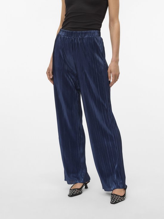 Model in een donkerblauwe, glanzende, wijde broek met plooien.