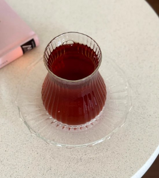 Klassiek theeglas met ribbels, gevuld met donkere thee, op een bijpassend glasen schoteltje.