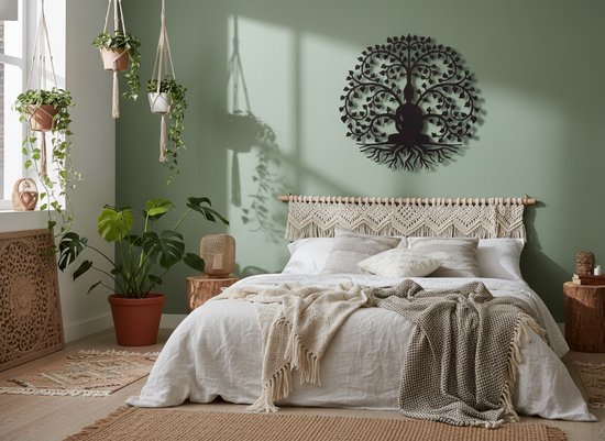 Zwarte Boeddha in een levensboom, metaal kunstwerk boven een bed met boho-stijl decoratie en planten.