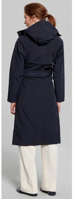 Vrouw met lange donkerblauwe jas met capuchon, ceintuur en witte broek, van achteren gezien.