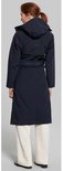 Vrouw met lange donkerblauwe jas met capuchon, ceintuur en witte broek, van achteren gezien.