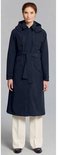 Vrouw in lange donkerblauwe jas met capuchon, ceintuur en witte broek, van voren gezien.