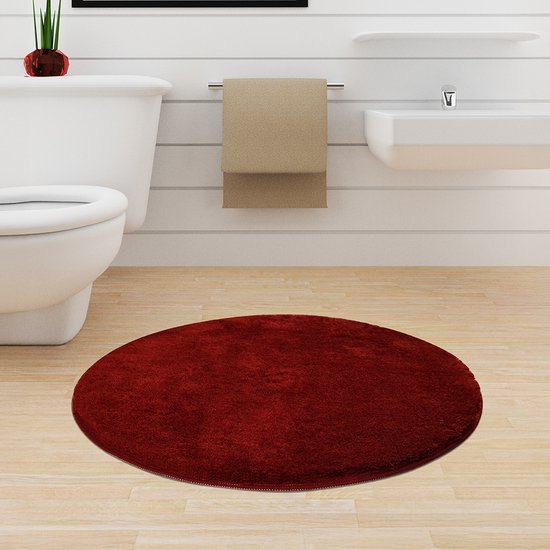 Rode, ronde, pluizige badmat op een houten vloer in een badkamer.