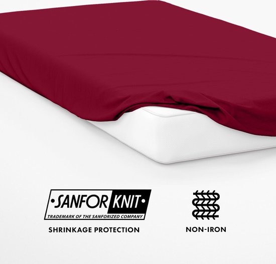 Een wijnrood hoeslaken dat op een matras ligt. Logo 'SANFOR KNIT' en tekst 'SHRINKAGE PROTECTION NON-IRON'.