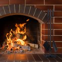 Zwart haardstel met schep, bezem en pook naast een brandende open haard.