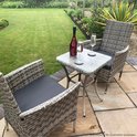 Twee grijze rotan stoelen met donkergrijze kussens en een glazen bistrotafeltje, met champagne op het tafeltje.