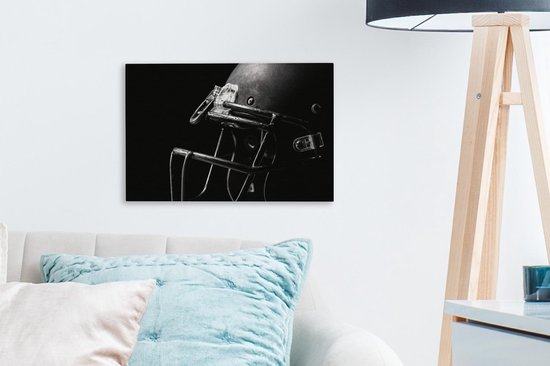 Un casque de football américain noir avec masque, sur un mur à côté d'un canapé avec coussins et d'une lampe.